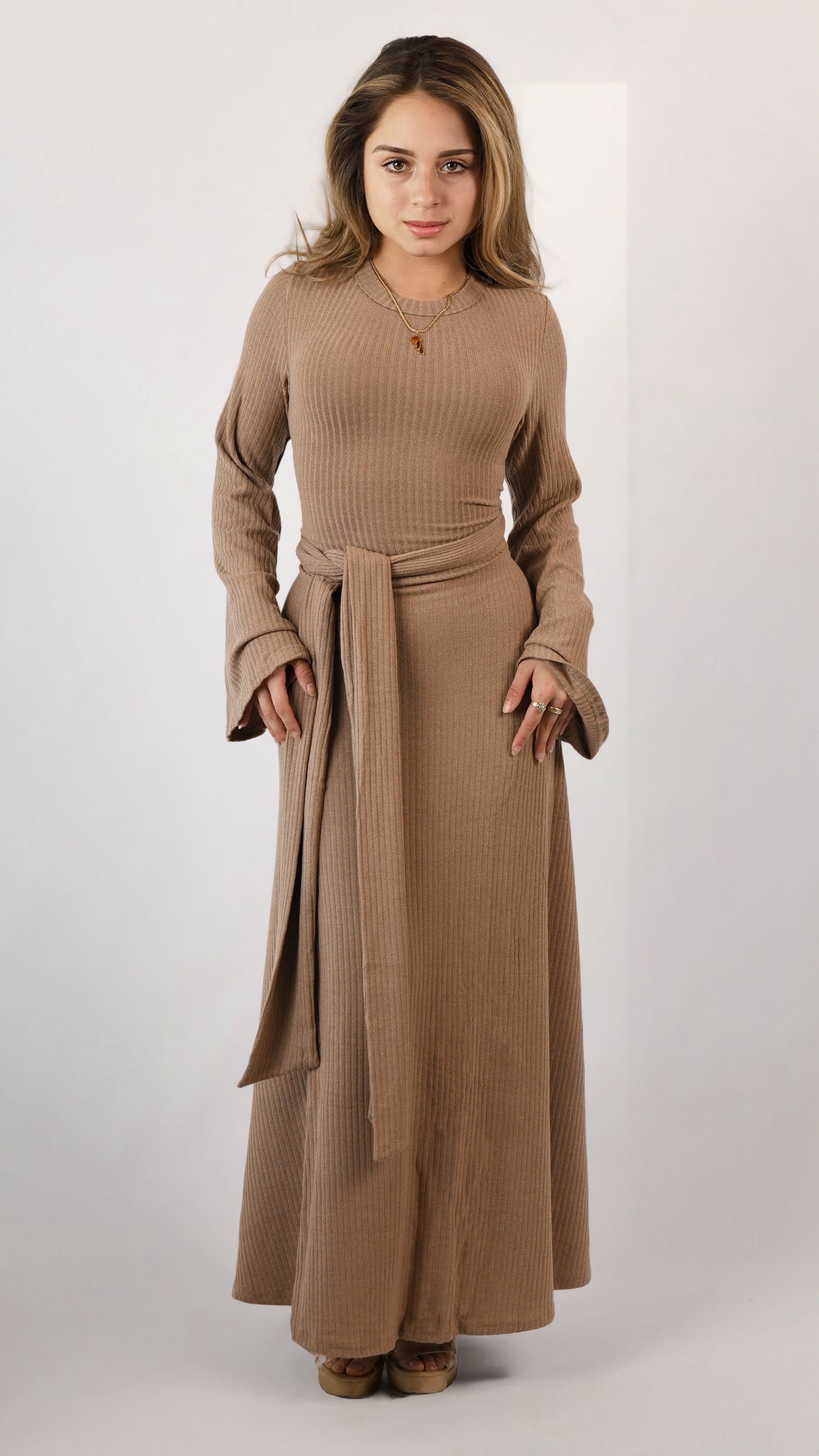 Woman wearing a long brown dress with a belt on a white background