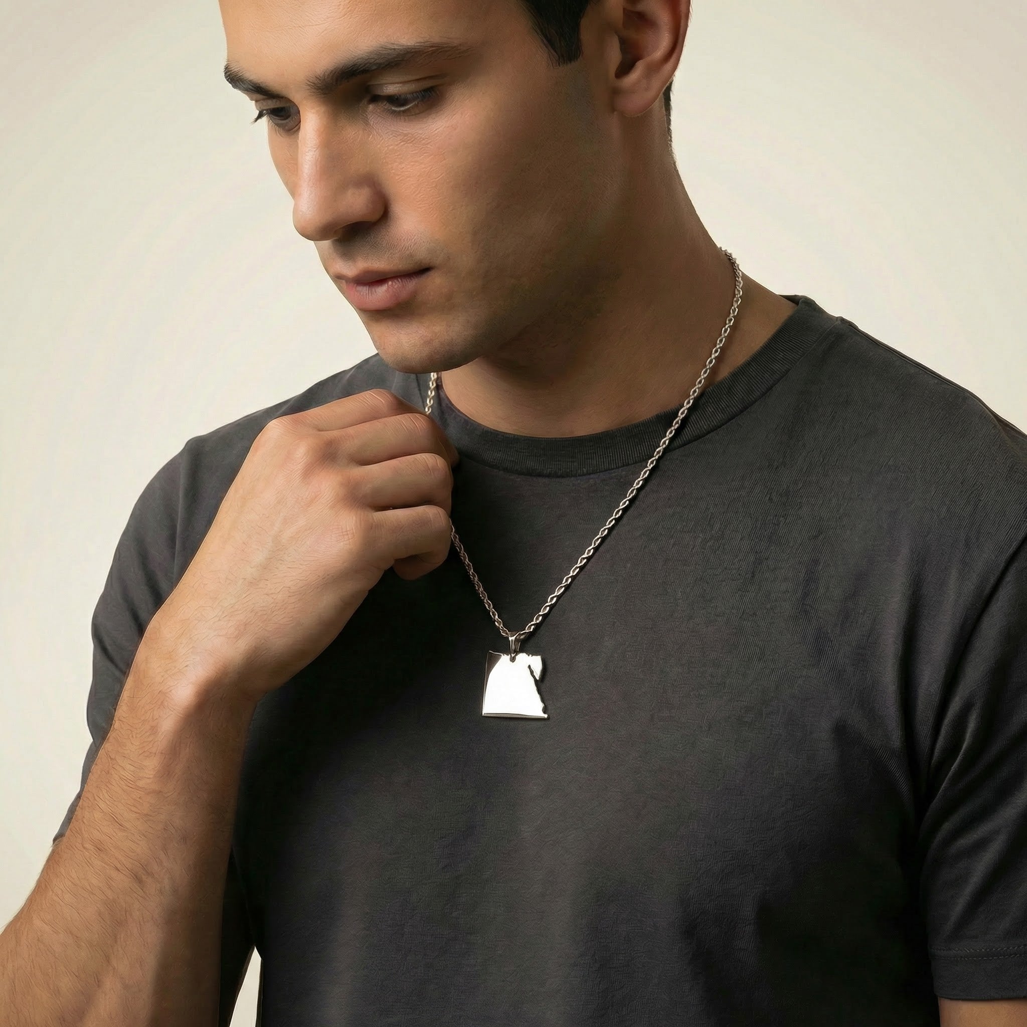 Man wearing a dark gray t-shirt with a necklace featuring a white pendant against a neutral background