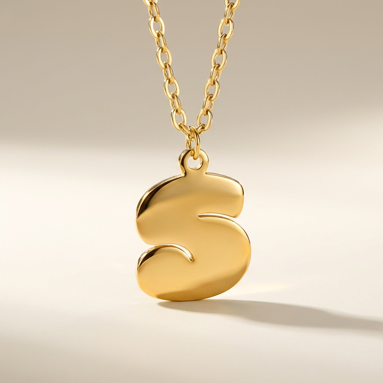 Gold necklace with a letter 'S' pendant on a beige background