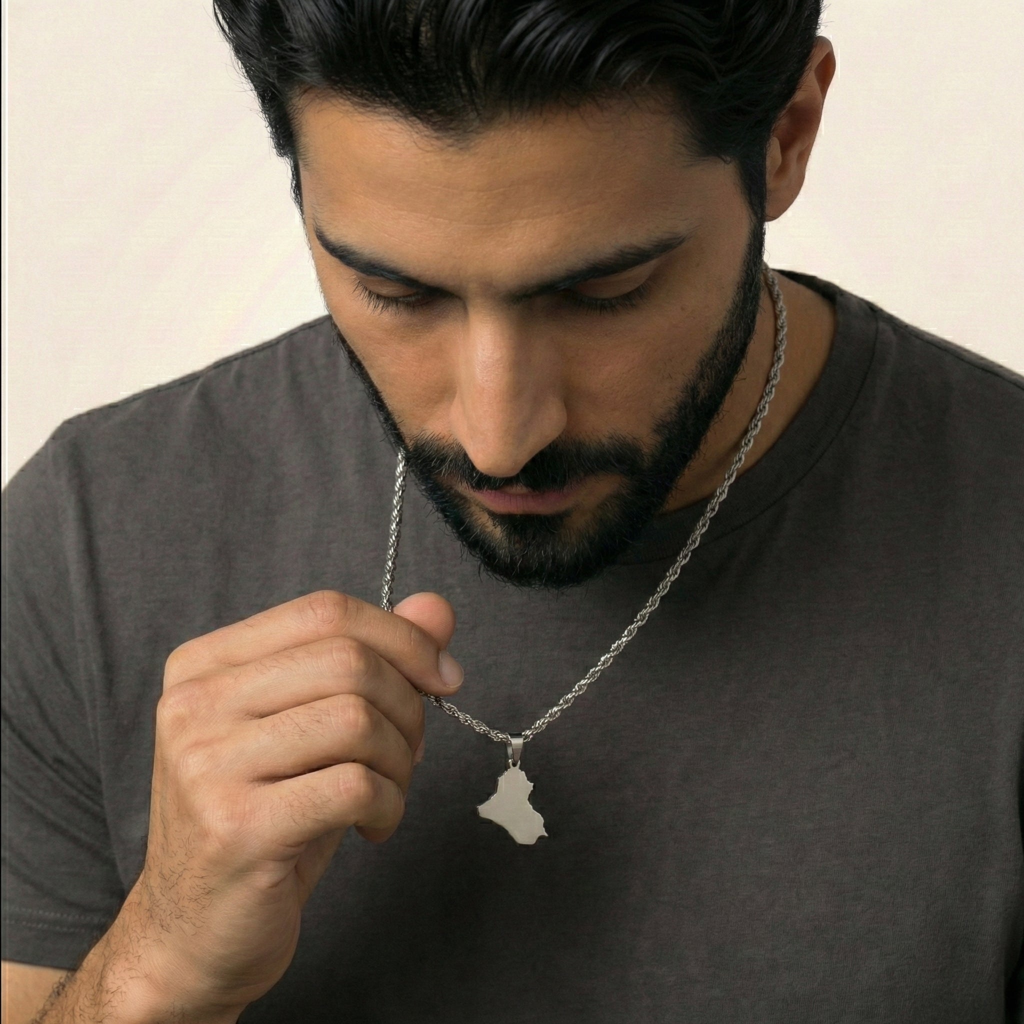 Man wearing a necklace with a pendant, looking at it.