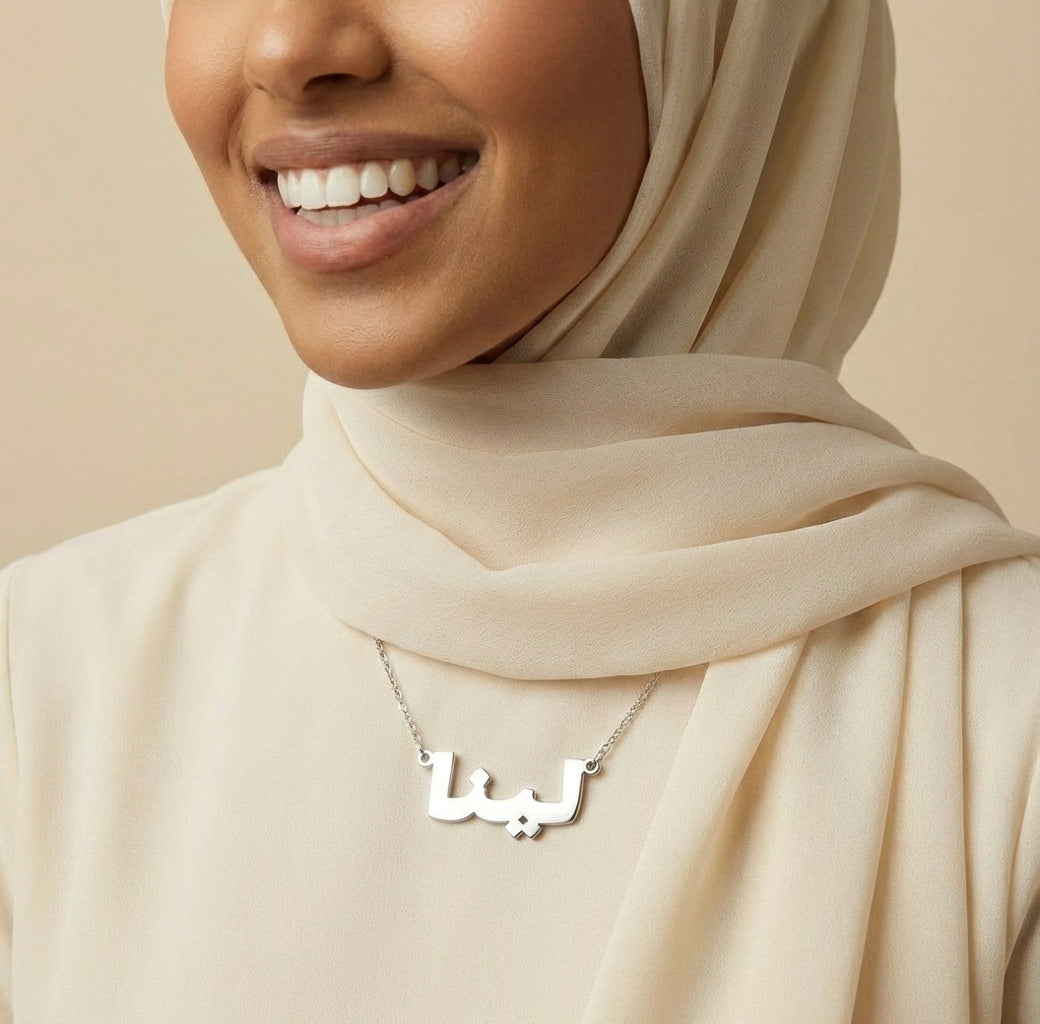 Woman wearing a hijab with a silver name necklace on a beige background