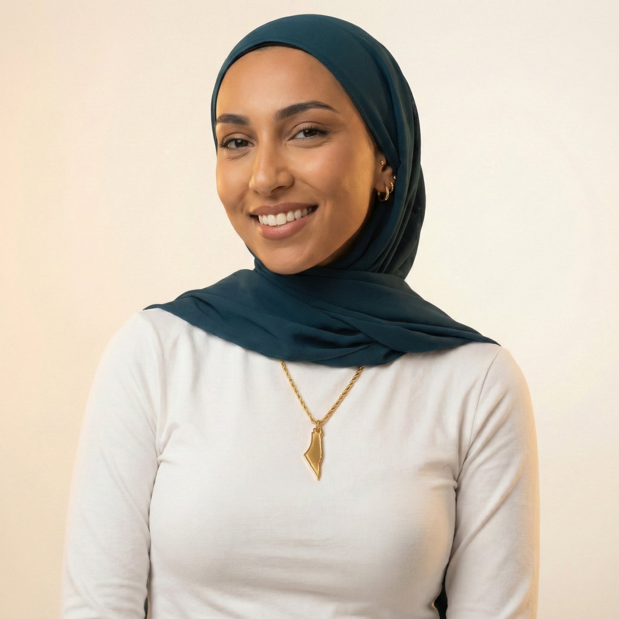 Woman wearing a teal hijab and gold necklace against a beige background