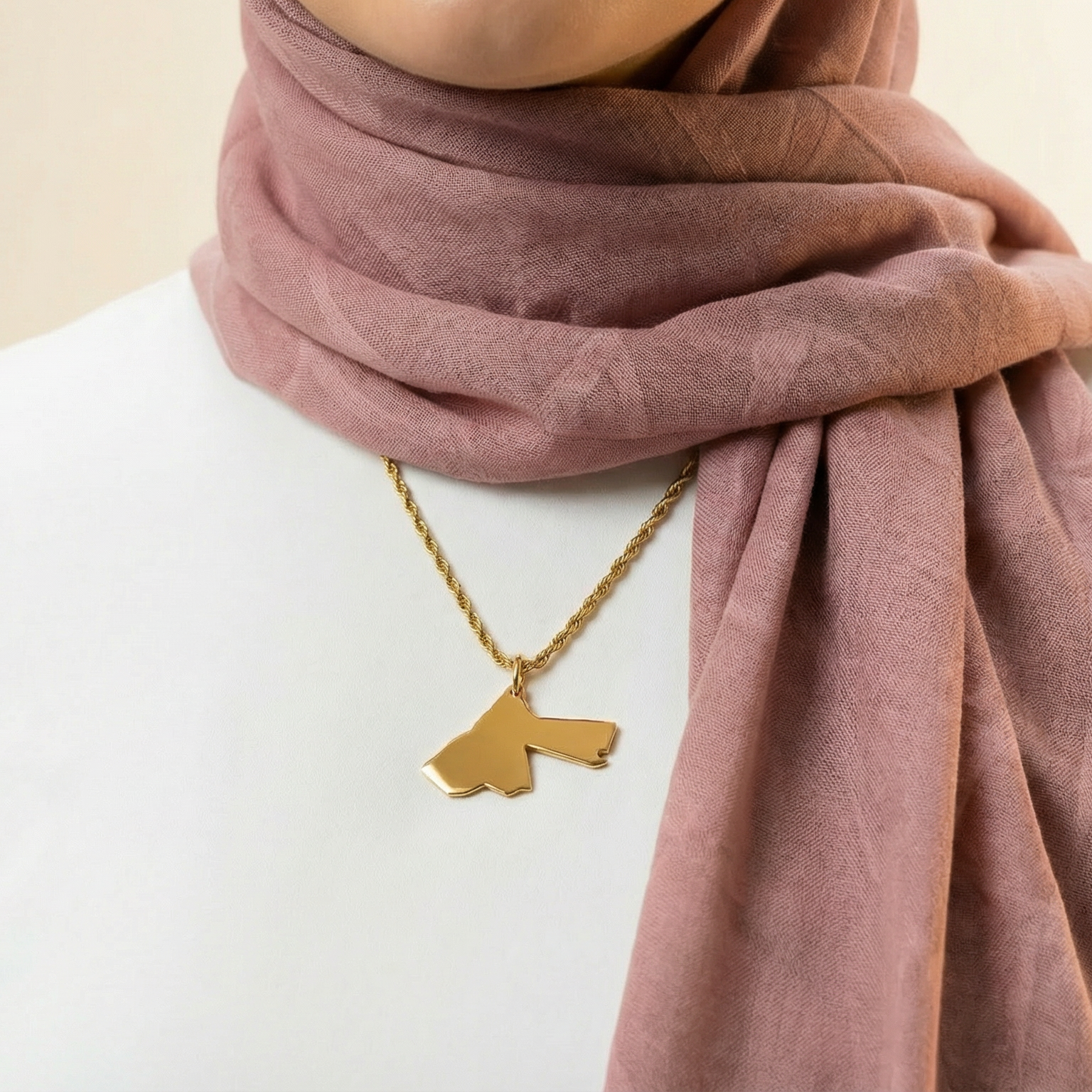 Person wearing a pink hijab and gold necklace with a pendant on a beige background