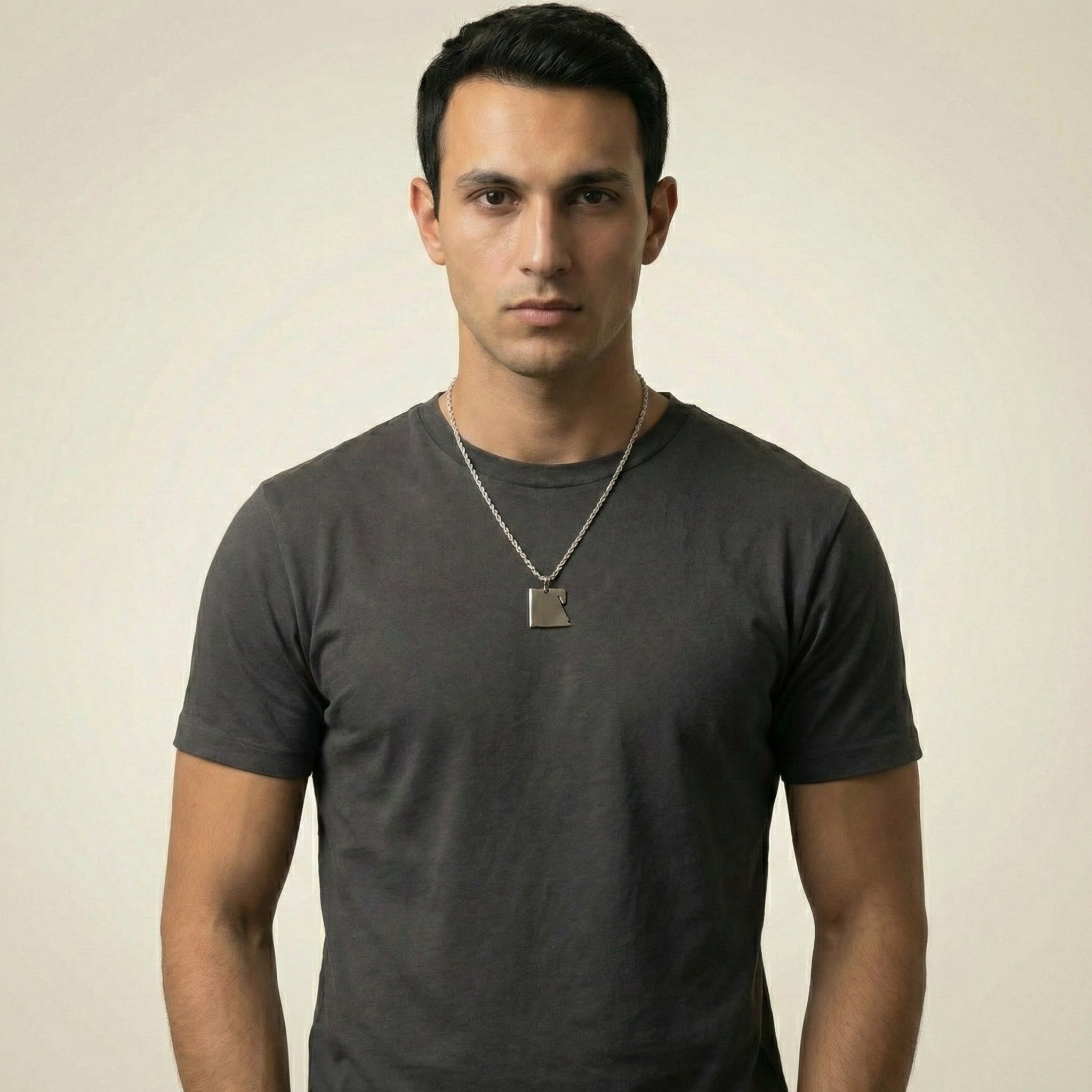 Man wearing a dark gray t-shirt with a necklace against a beige background