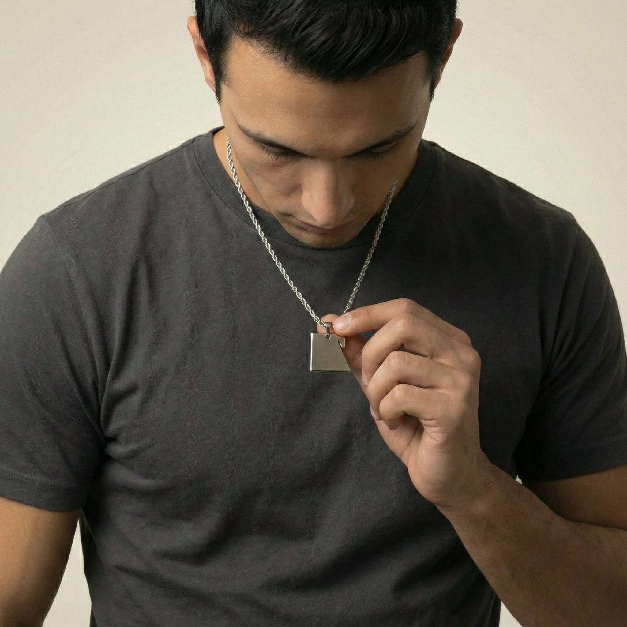 Man wearing a dark gray t-shirt holding a silver necklace with a pendant.
