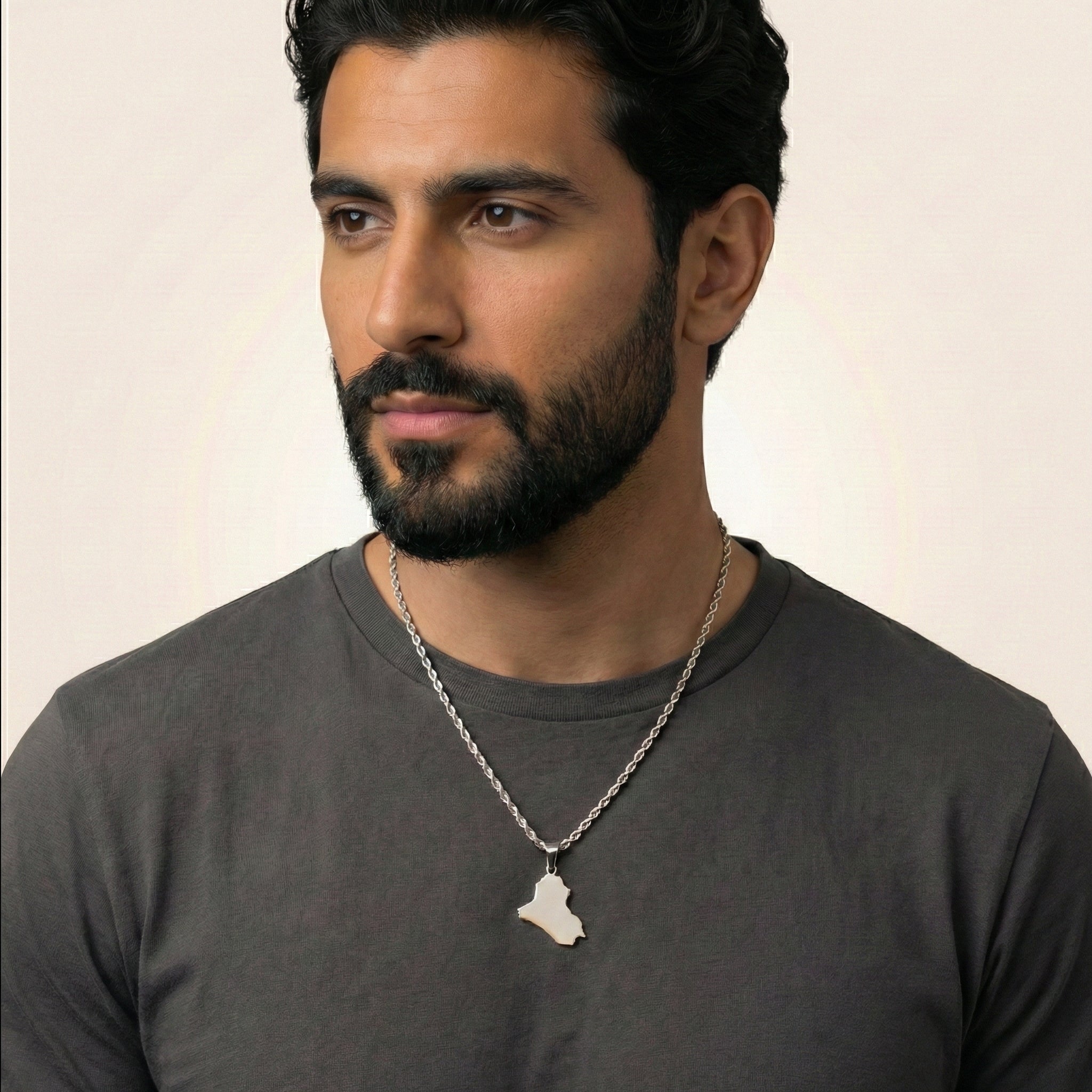 Man wearing a dark gray shirt and a necklace with a pendant against a plain background