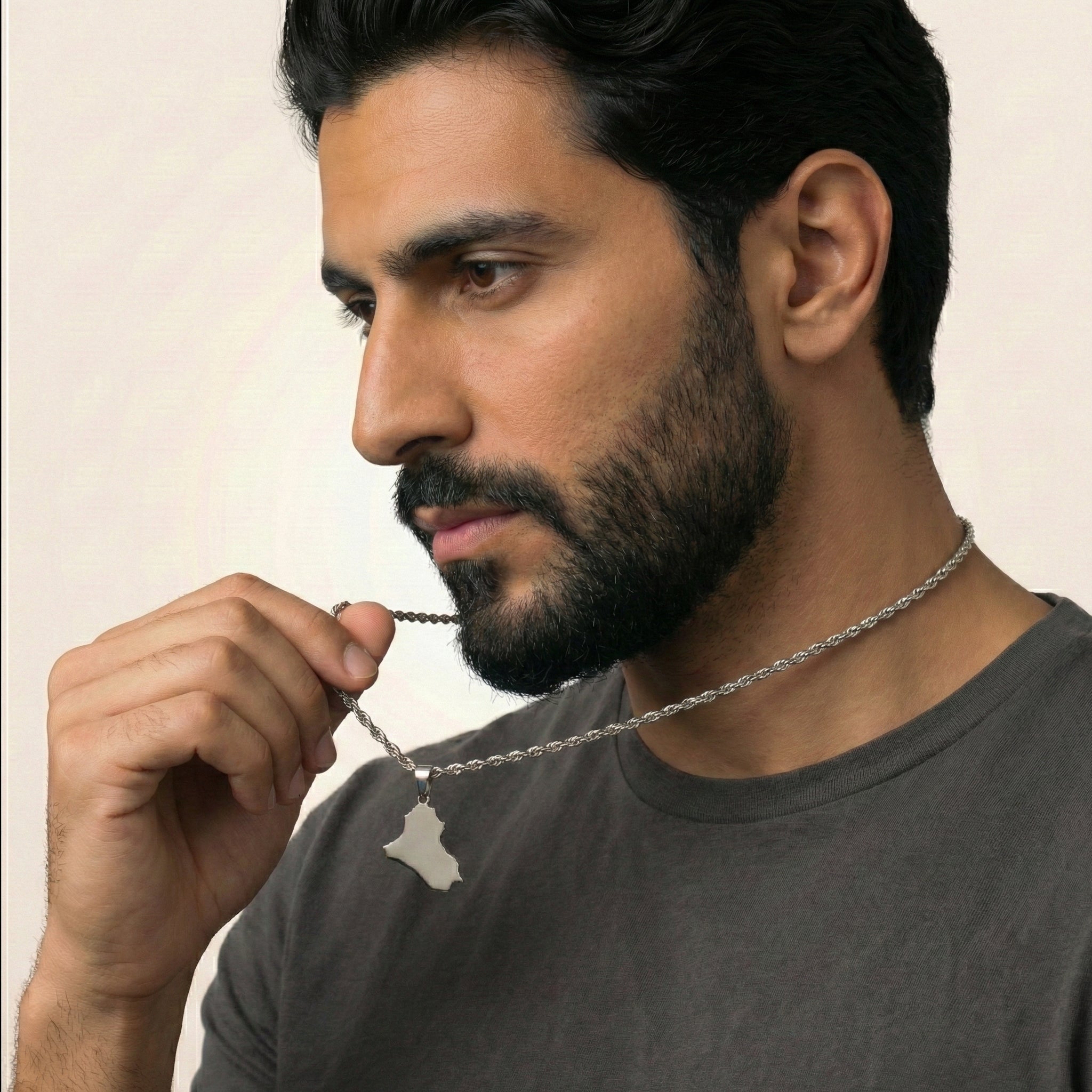 Man holding a necklace with a pendant, wearing a gray shirt against a beige background