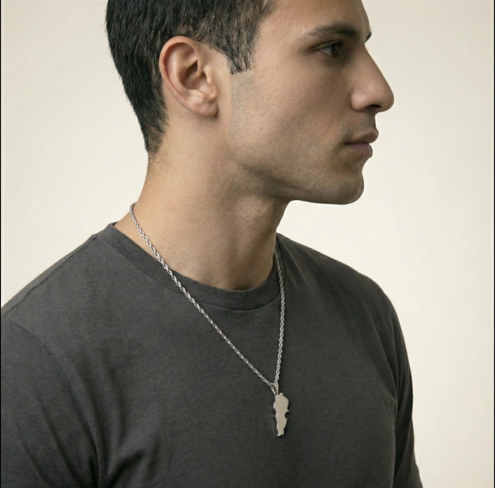 Man wearing a dark gray shirt and a necklace with a lebanon pendant on a plain background