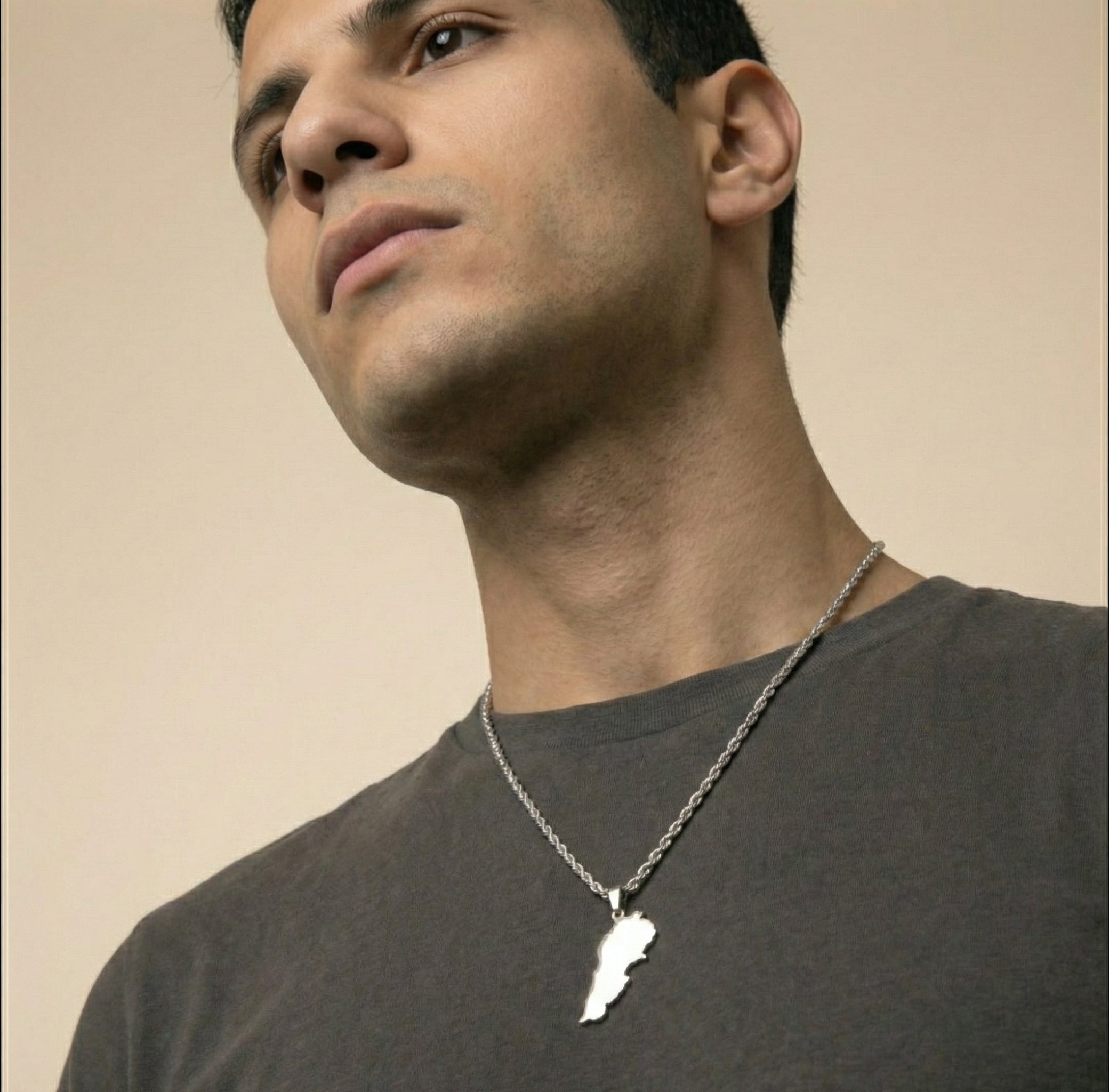 Man wearing a necklace with a lebanon pendant against a beige background