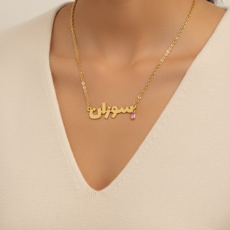 Gold necklace with name pendant on a person wearing a beige top