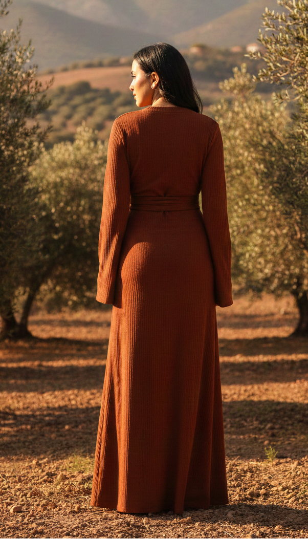 Woman in a rust-colored dress standing in an olive grove with mountains in the background