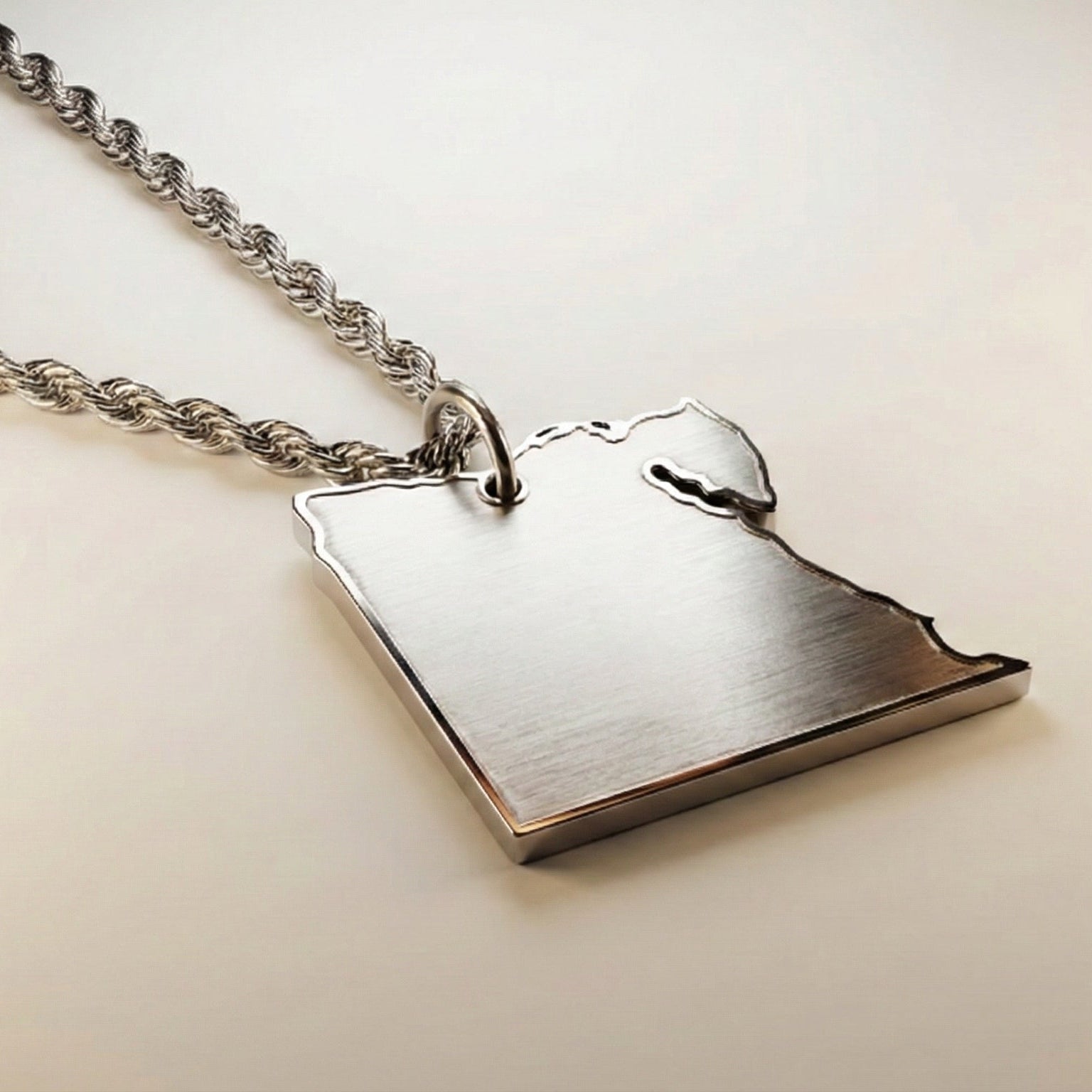 silver necklace with a pendant shaped like the country of egypt on a light beige background