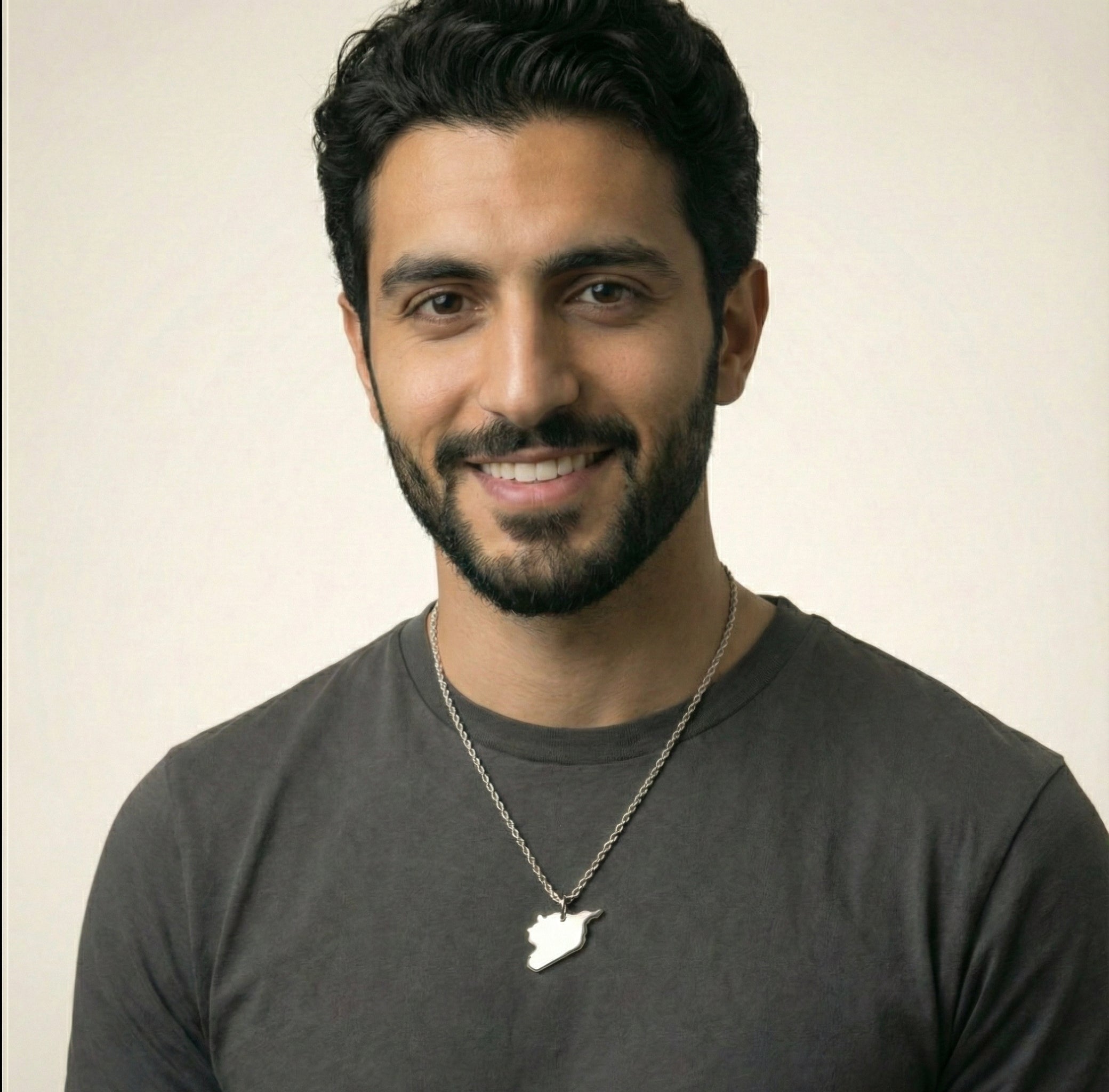 Man wearing a dark gray t-shirt with a necklace against a plain background