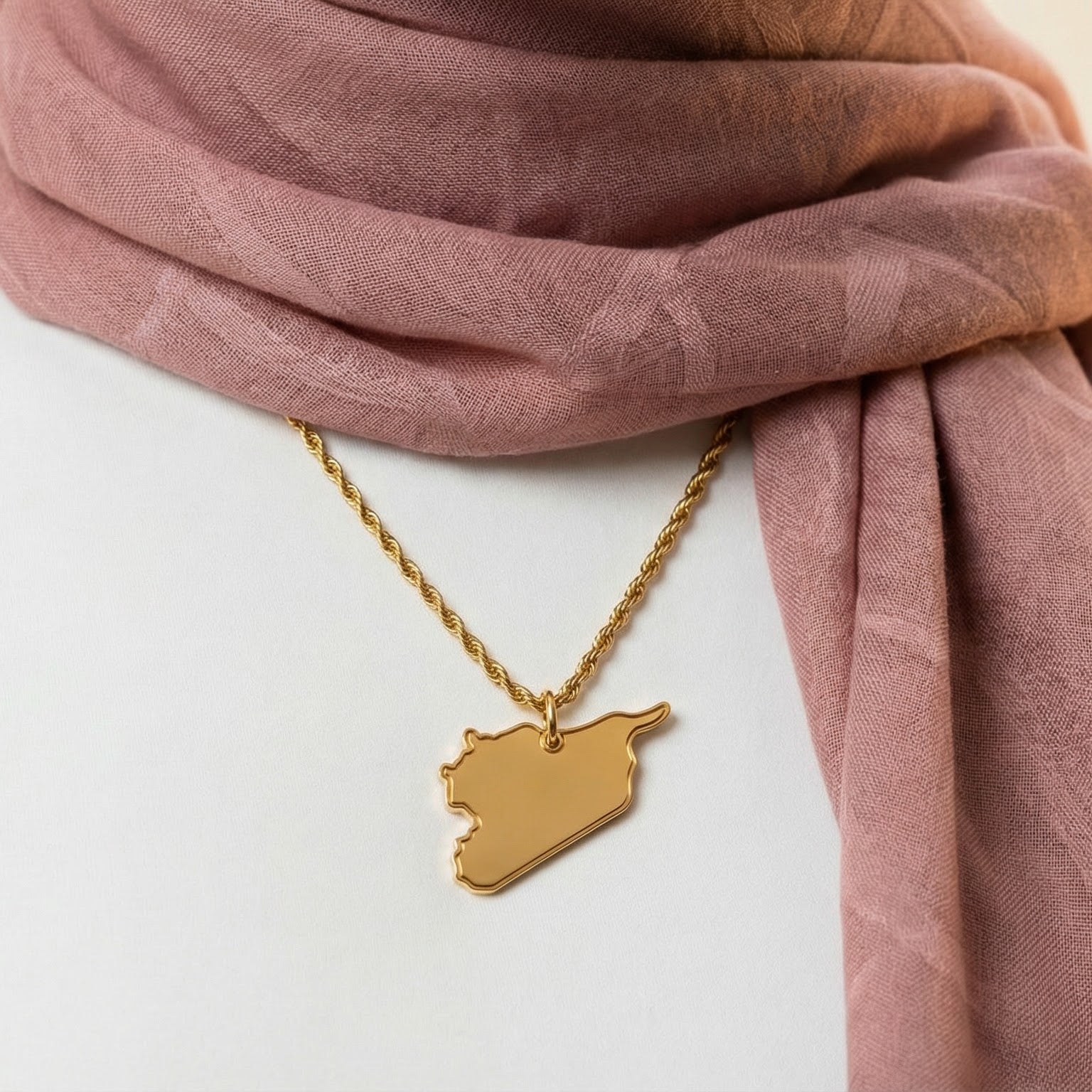 Person wearing a gold necklace with a syria-shaped pendant and a pink scarf.