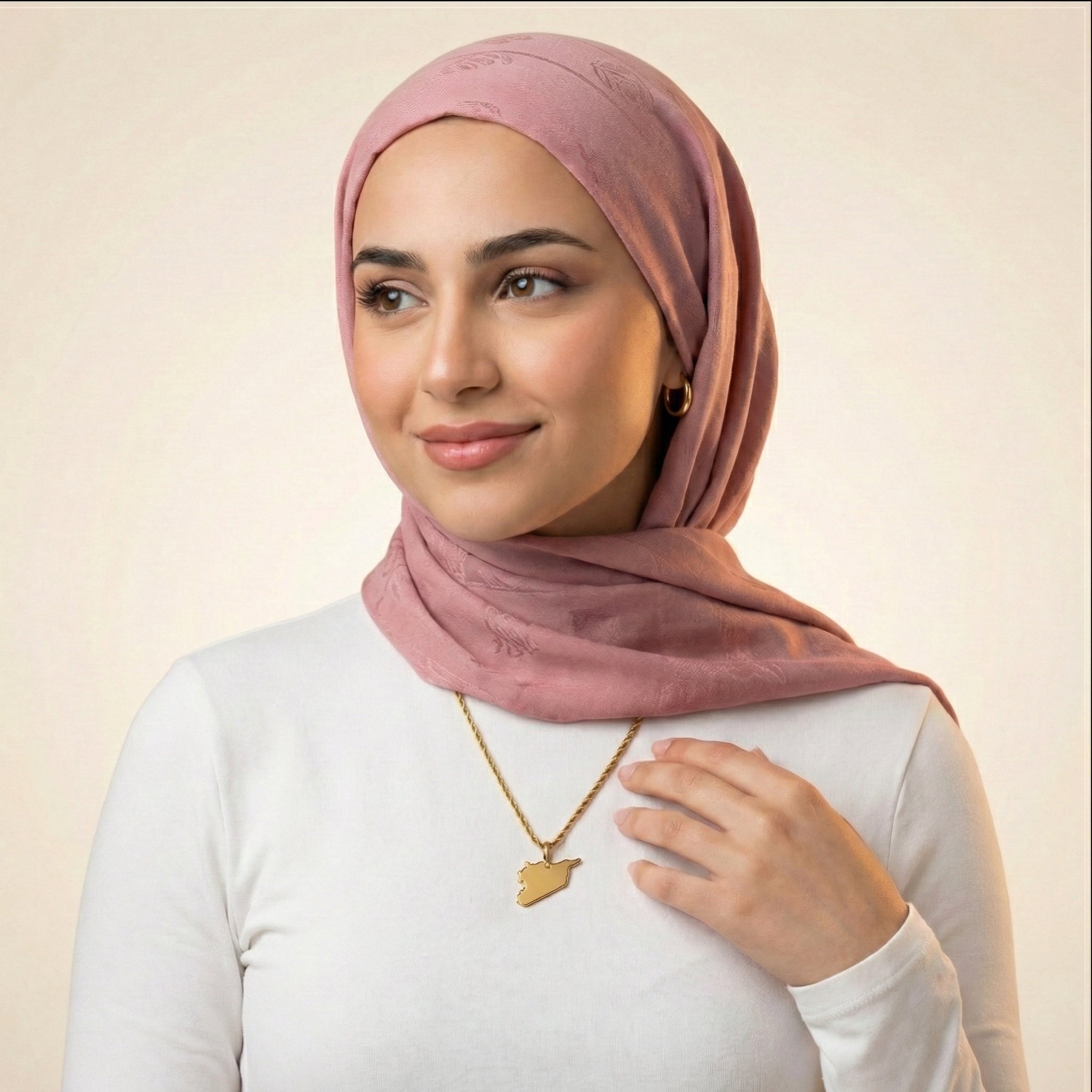 Woman wearing a pink hijab and gold necklace against a beige background