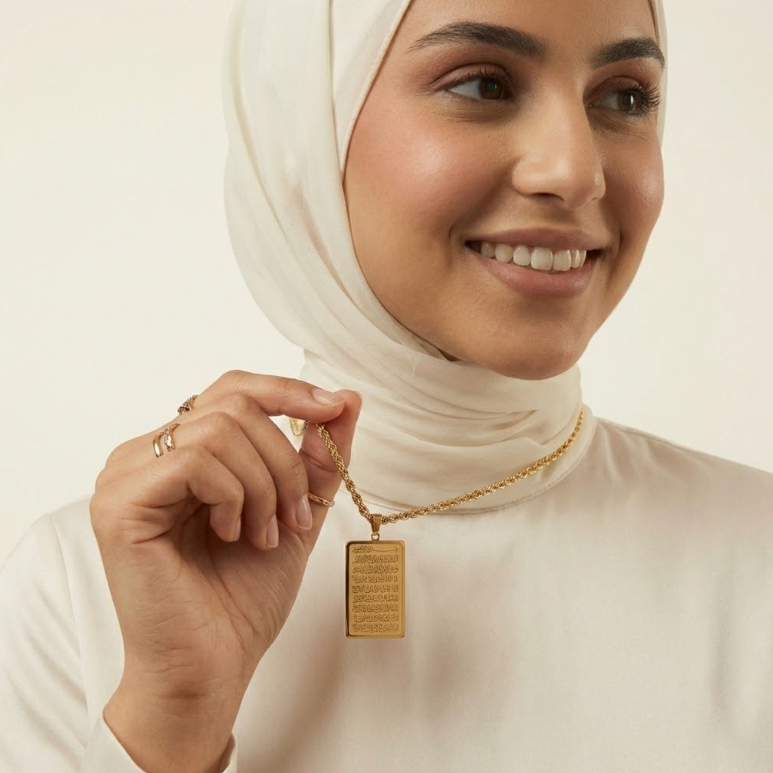 Woman wearing a gold ayatul kursi necklace with a pendant, smiling against a plain background